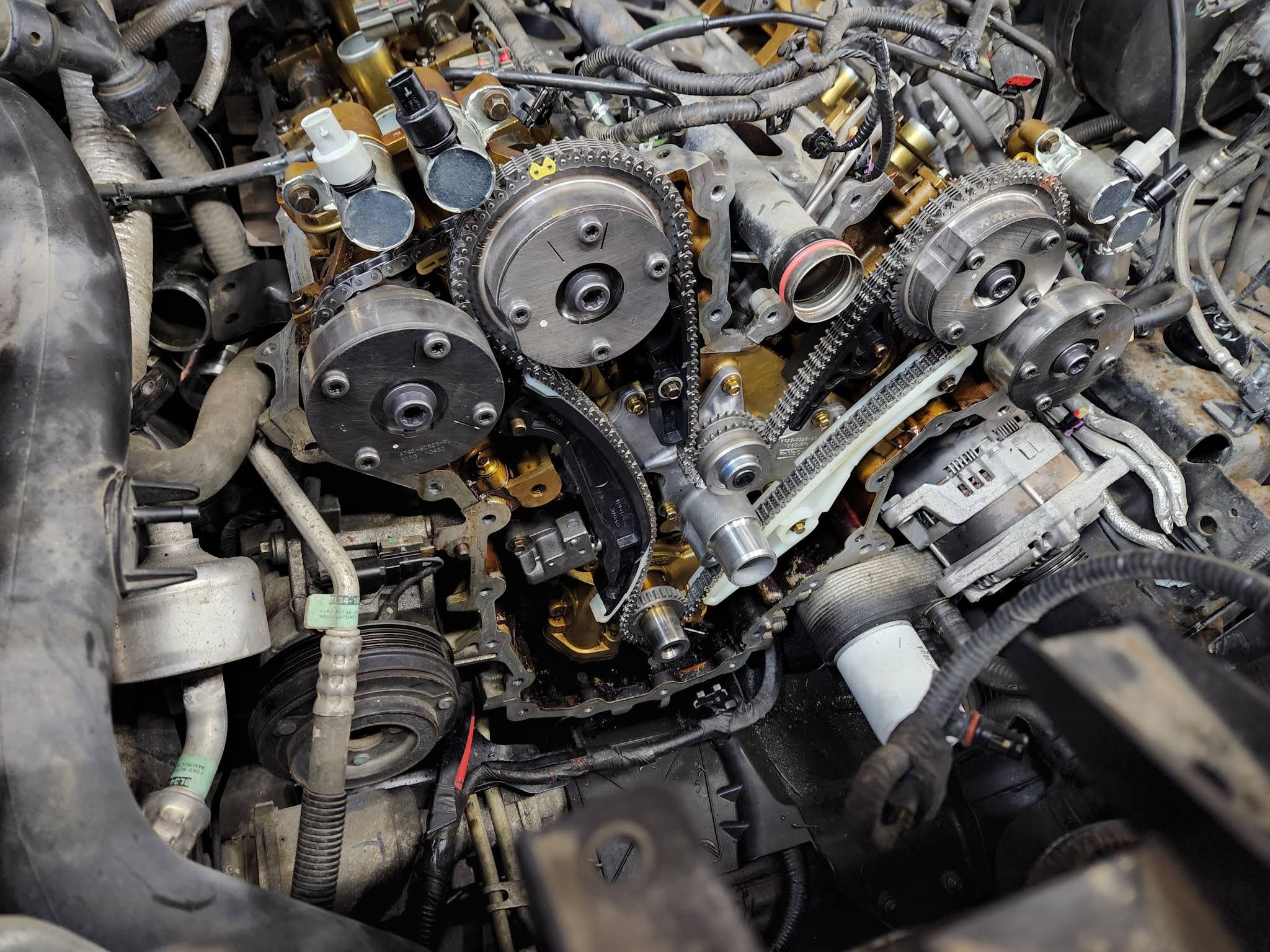 Disassembled engine bay showing timing chains, cam phasers, and accessory components